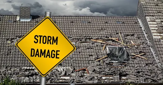 Yellow damage warning sign in front of storm damaged roof of house